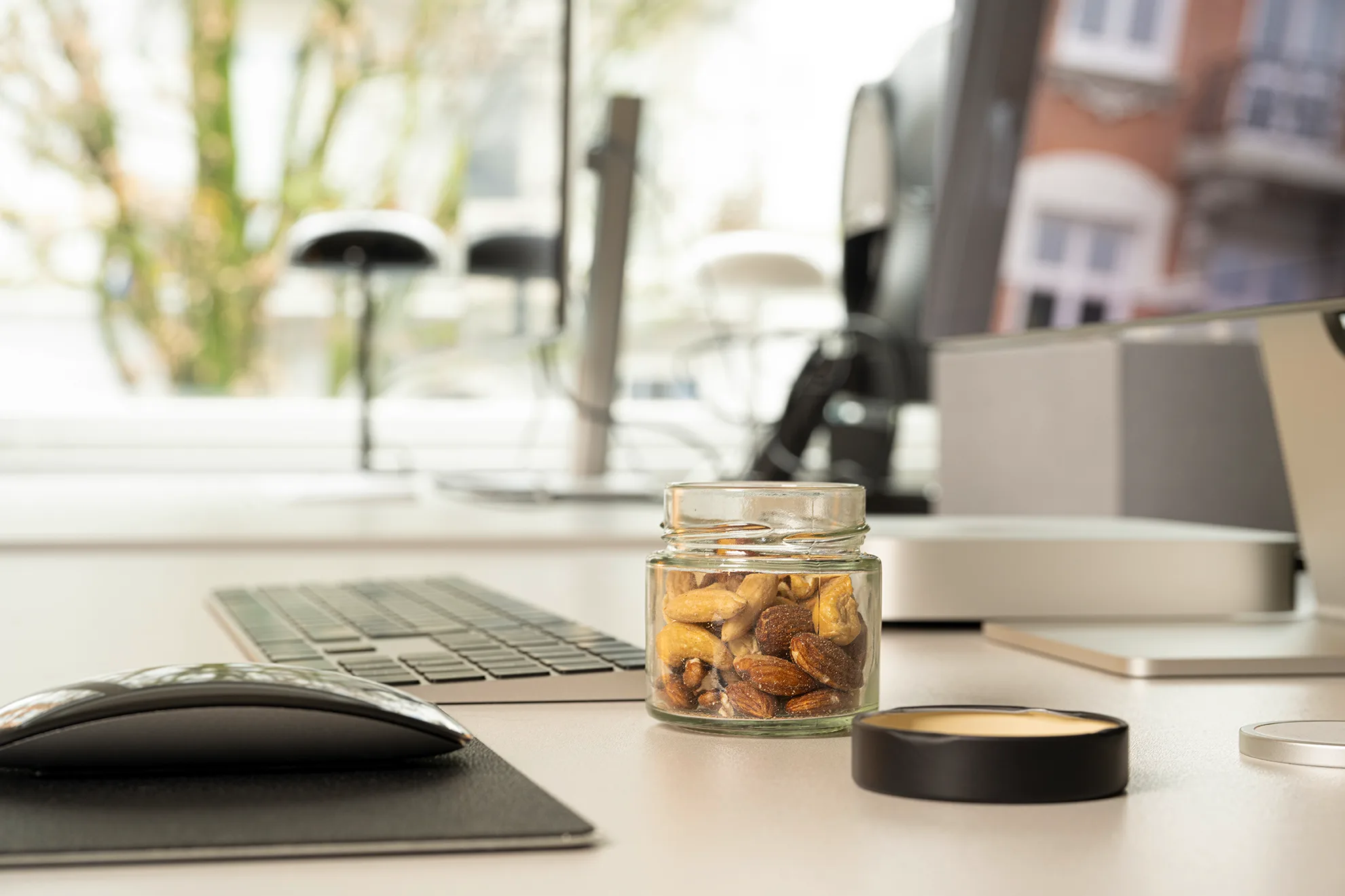Portionierungsglas mit Nüssen auf einem Schreibtisch neben Tastatur und Bildschirm