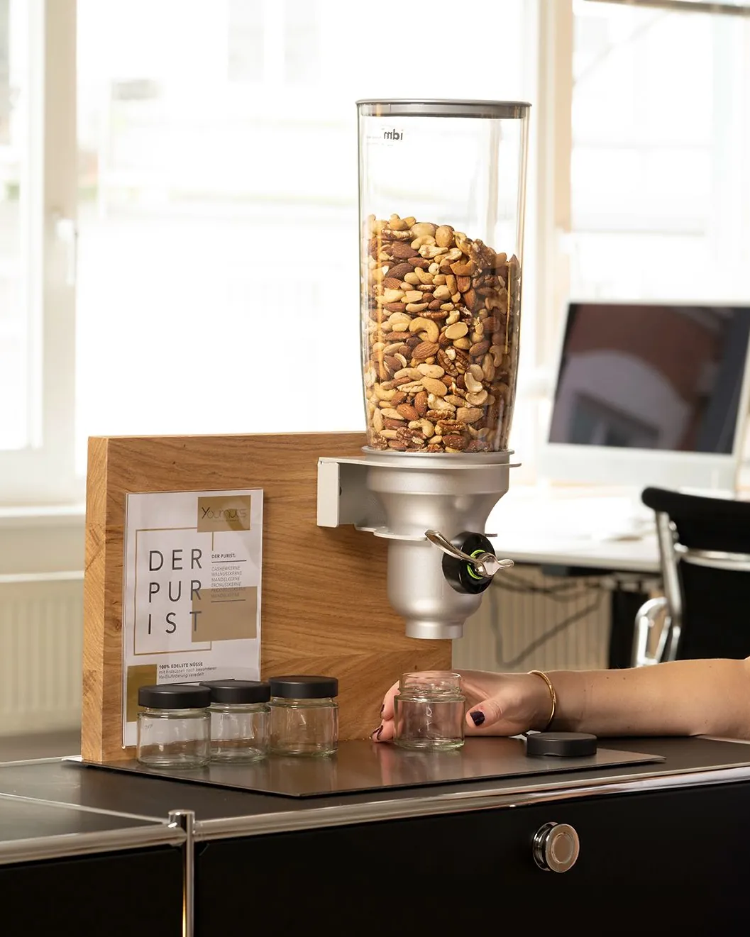 Eine Hand stellt ein Portionsglas unter den Nussspender, daneben weitere Gläser mit Deckel